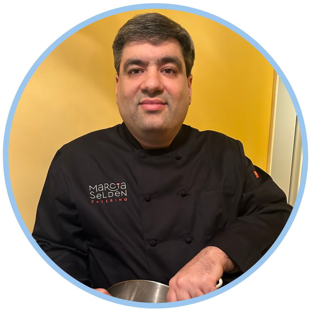 Richard wearing a black chef's jacket and holding a bowl and whisk.